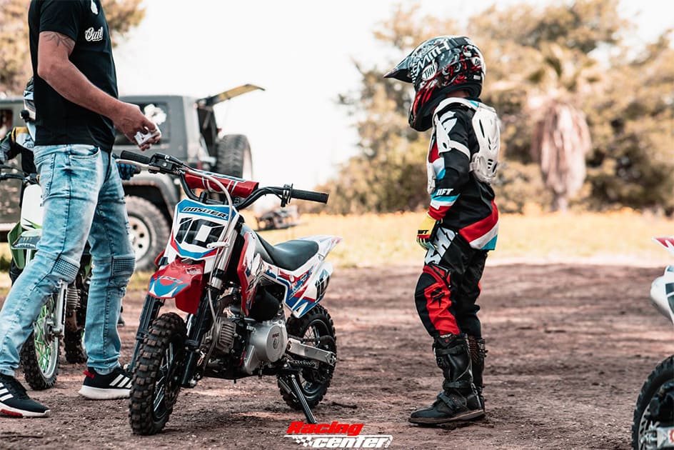 A kid motorcross rider is ready to ride a mini dirt bike under the suspervision of an adult